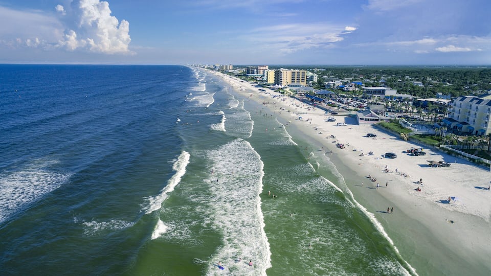 A coastal city with a wide beach, ocean waves, and buildings along the shore.