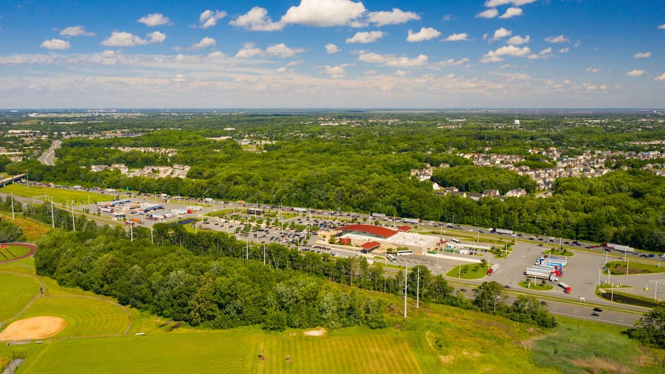 An aerial view of a town with a large parking lot, green fields, and scattered buildings.