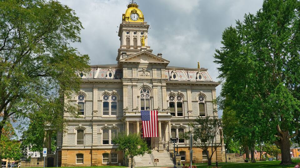A historic building with a clock tower, an American flag, and a statue on the roof.