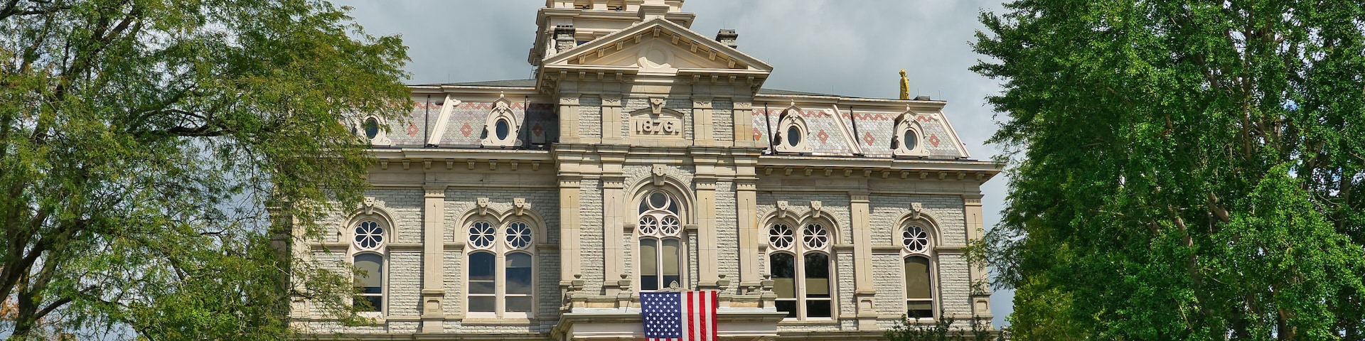 Um edifício histórico com uma torre de relógio, uma bandeira americana e uma estátua no telhado.