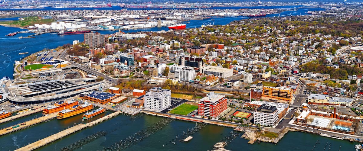 A coastal cityscape with a prominent harbor, including a large cruise ship docked at the pier, and a dense urban area with various buildings and greenery.