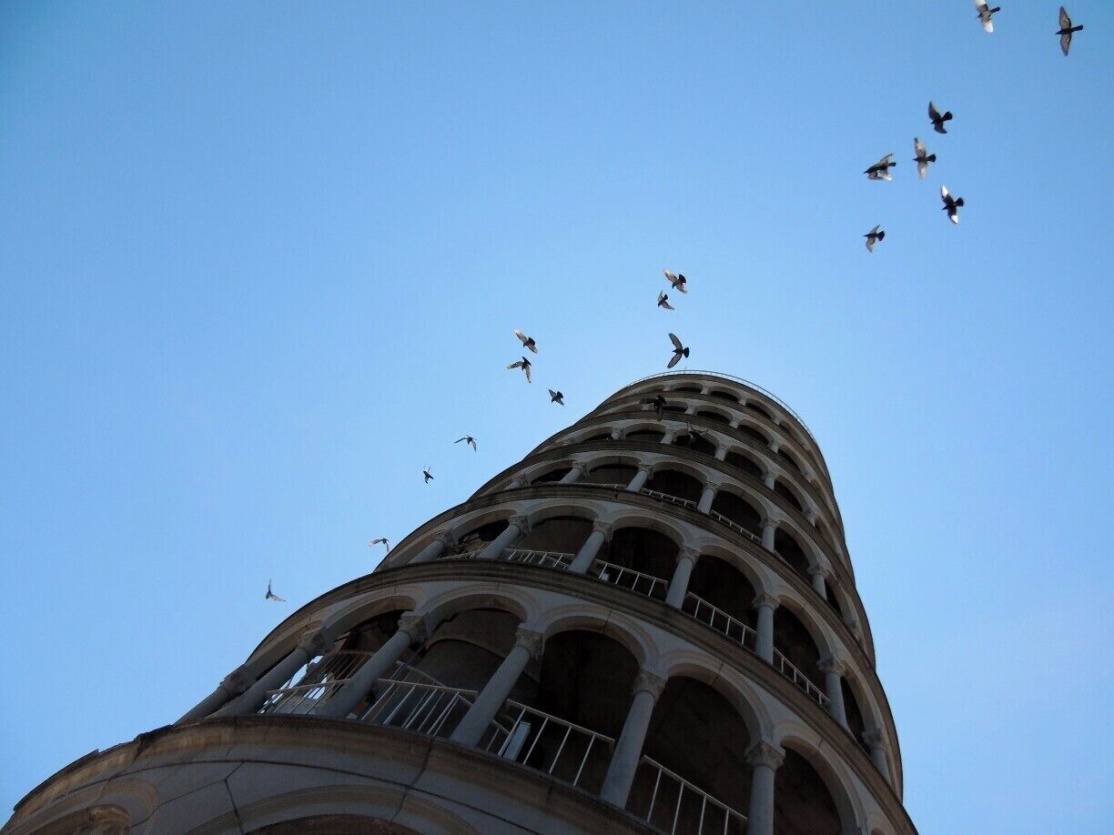 A tower with multiple arches and a flock of birds flying around it.