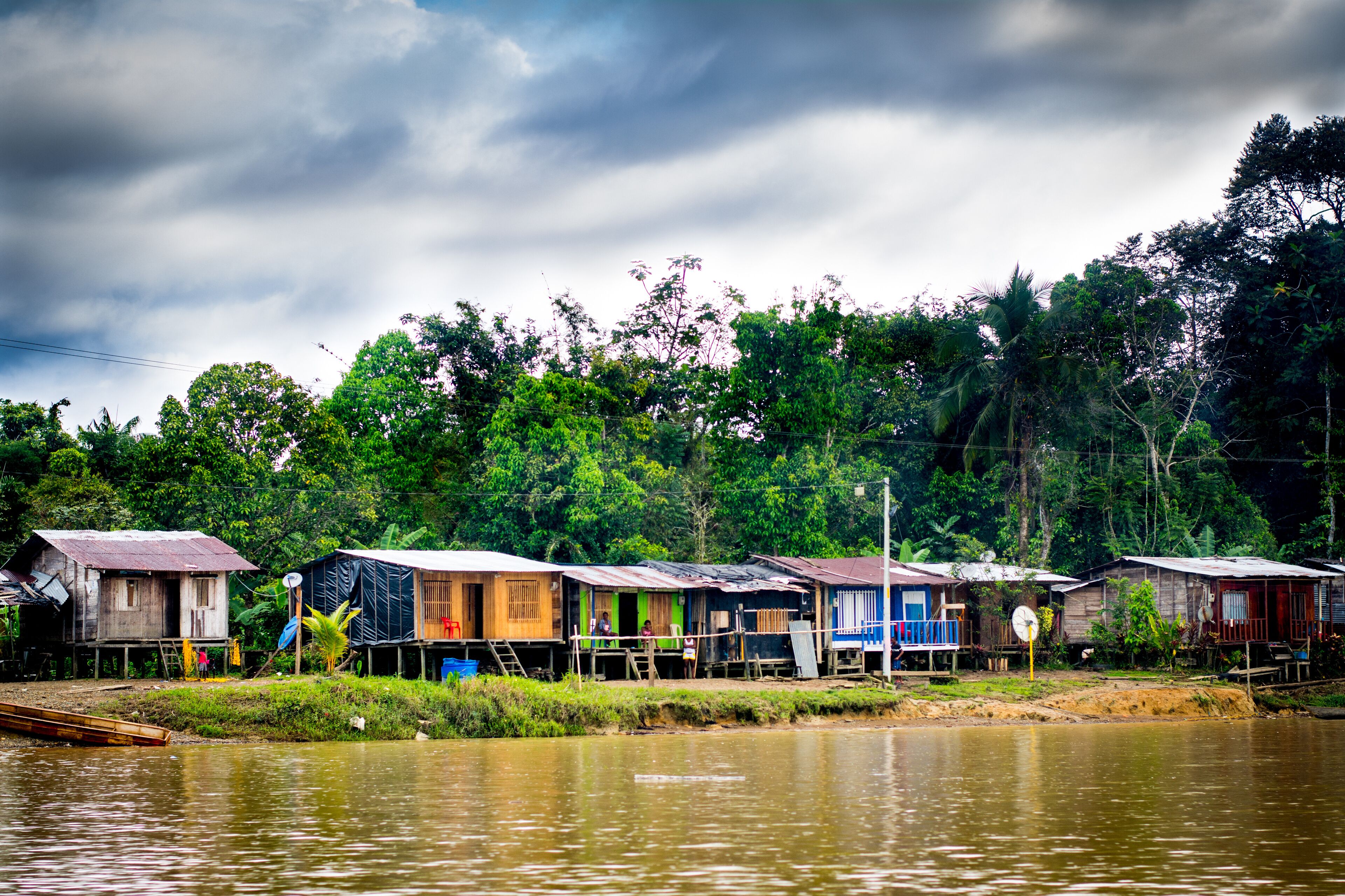 A riverfront with floating houses, surrounded by lush greenery and a cloudy sky.
