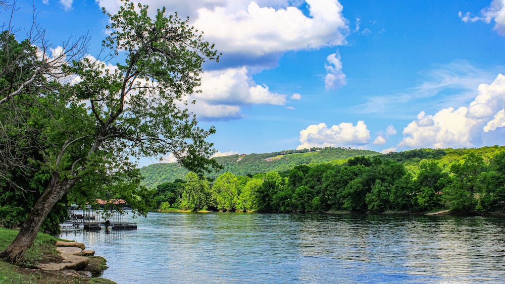A river with a dock, surrounded by lush greenery and hills.