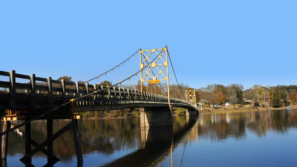 A suspension bridge over a calm river with a clear sky.