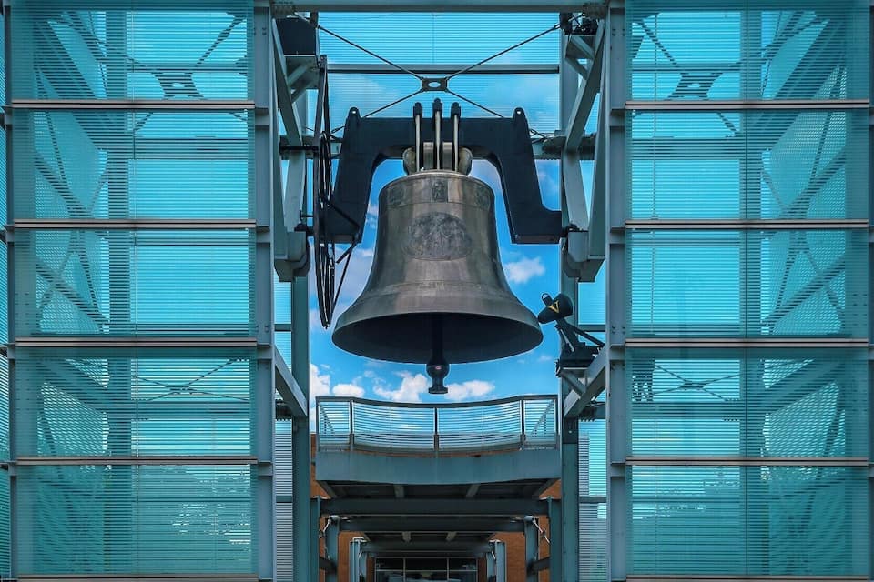 A large bell suspended in front of a modern glass building.