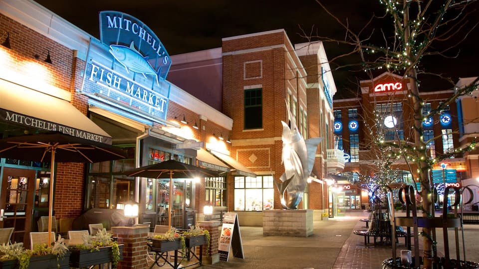 A nighttime view of Mitchell's Fish Market with illuminated signage, outdoor seating, and a statue in the center.