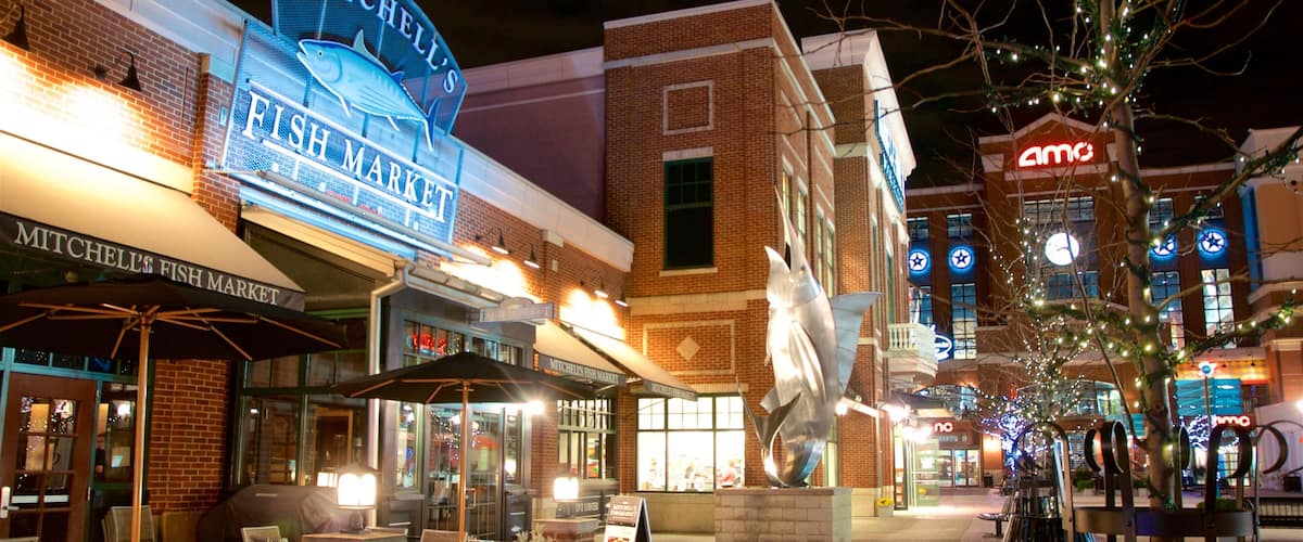 A nighttime view of Mitchell's Fish Market with illuminated signage, outdoor seating, and a statue in the center.