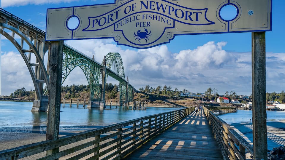 A wooden pier leading to a bridge with a sign reading 'The Port of Newport Public Fishing Pier.'
