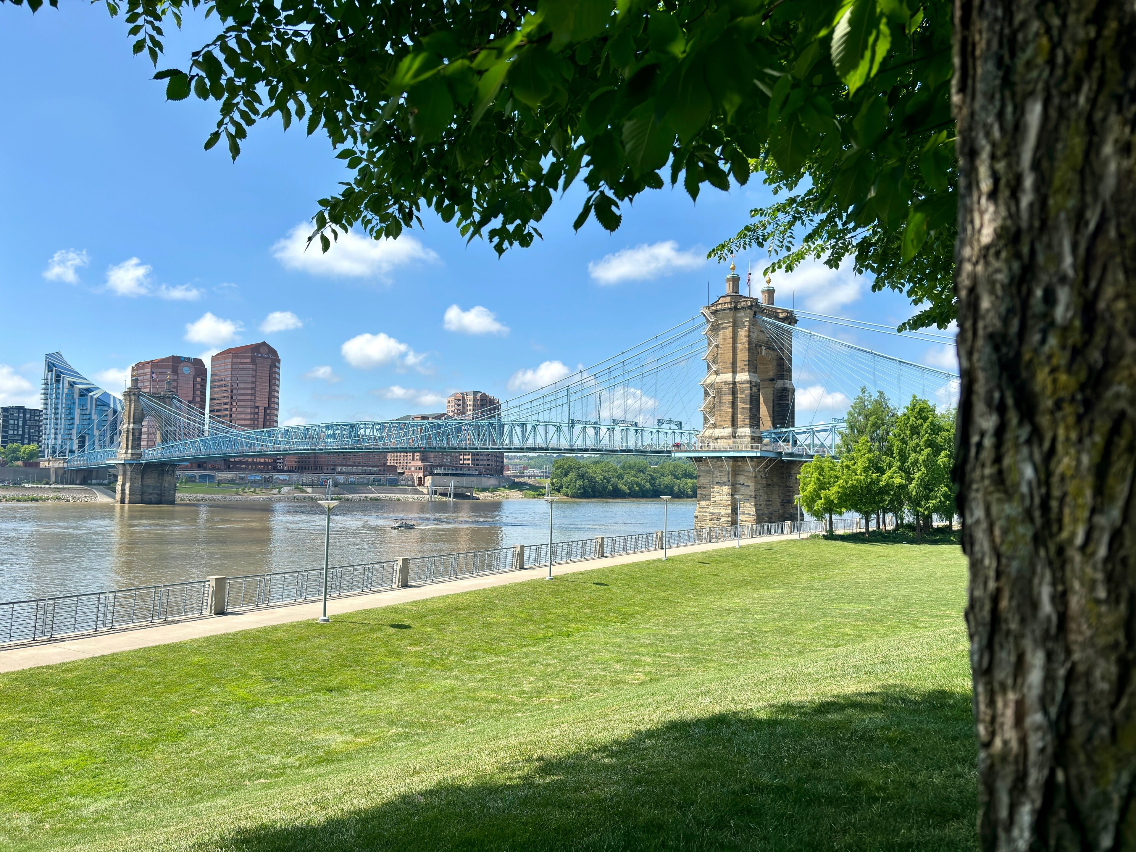 A suspension bridge over a river, a stone tower, and a grassy park area with trees.