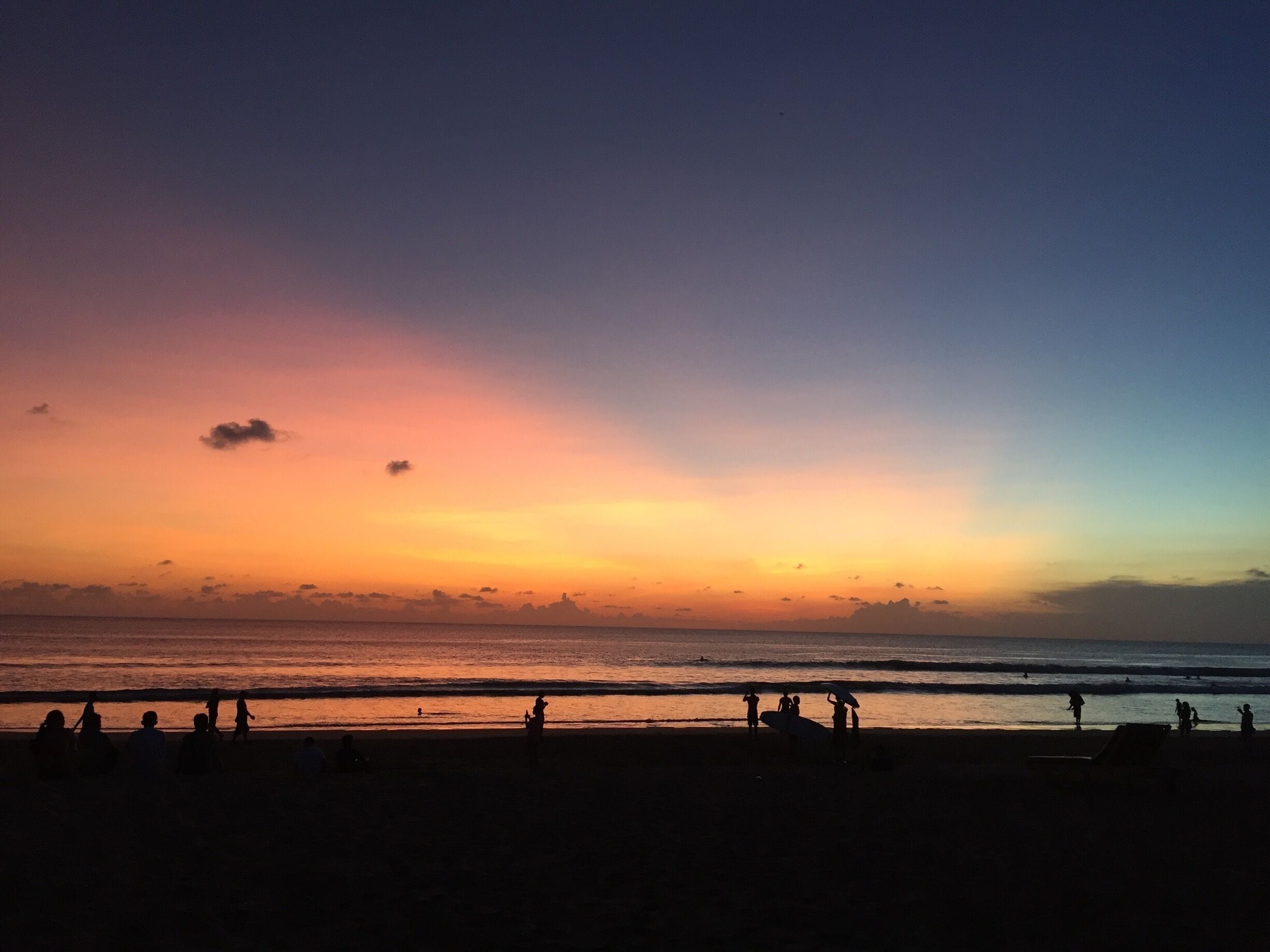 Een strand bij zonsondergang met silhouetten van mensen en golven.