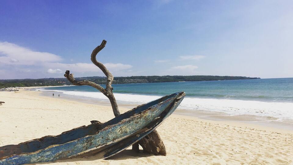 A beach with a weathered boat and a tree trunk.