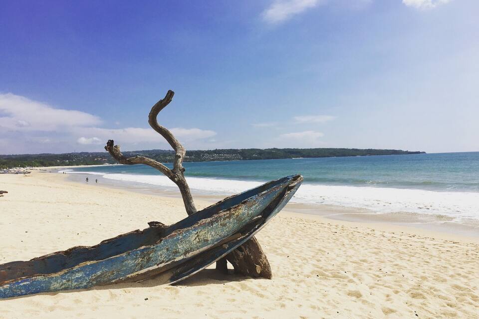 A beach with a weathered boat and a tree trunk.
