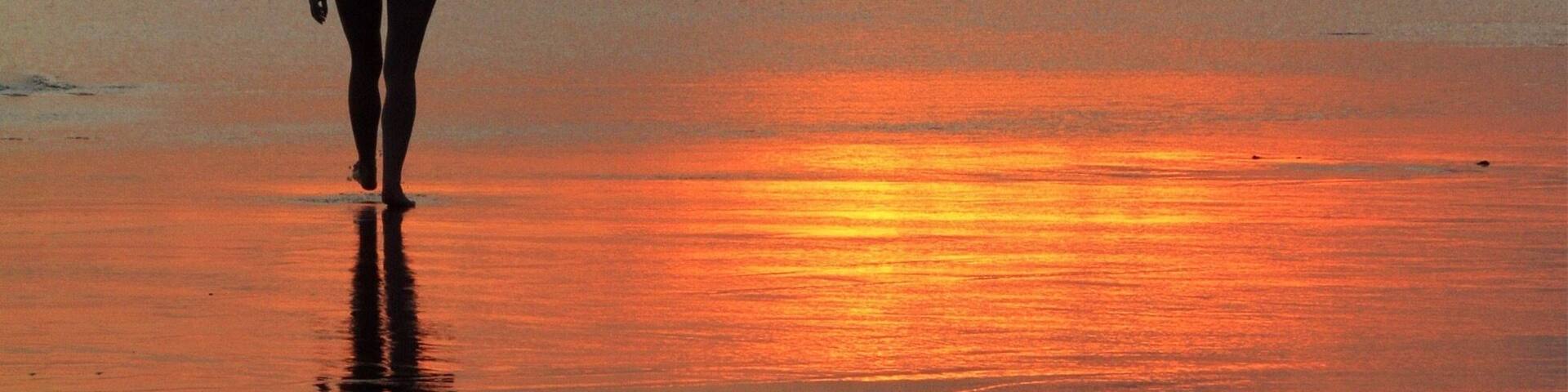 A person walking on a beach during sunset with waves in the background.