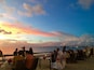 A beachside restaurant with tables and chairs under a sunset sky.