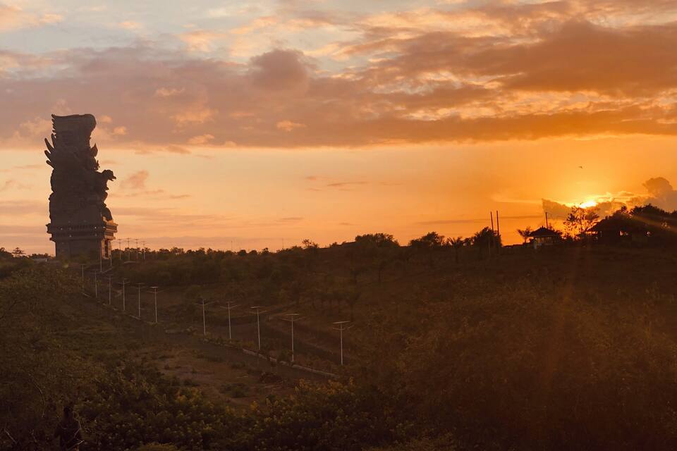 Een zonsondergang boven een landschap met een groot standbeeld en windturbines.