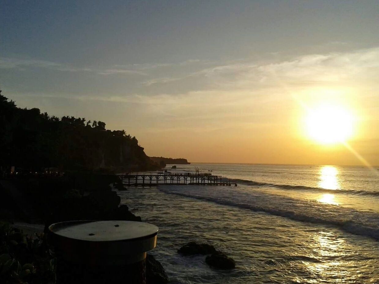 A sunset over a beach with a pier extending into the water.