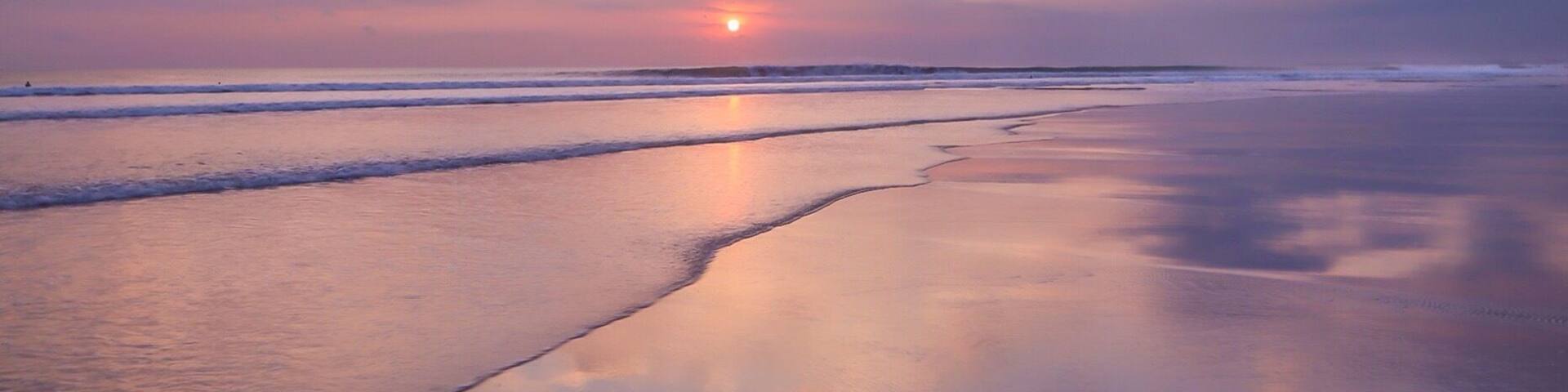 A beach at sunset with calm waves and a clear sky.