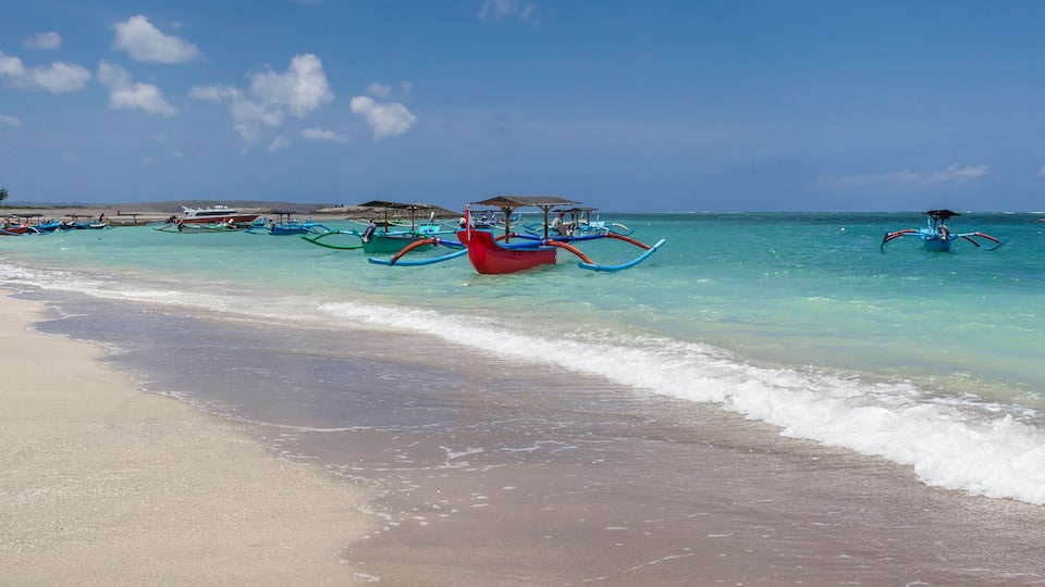 A beach with clear turquoise waters, several traditional boats, and a sandy shore.
