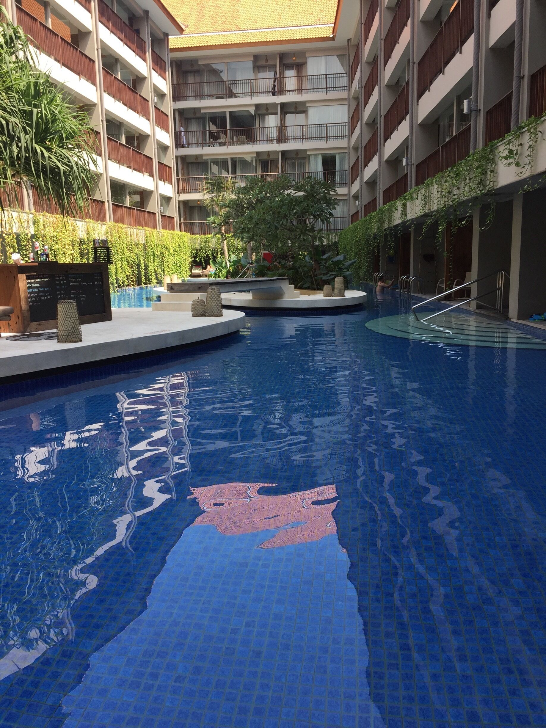 Una piscina interior con suelo de baldosas, rodeada por un edificio de varios pisos con balcones y vegetación.
