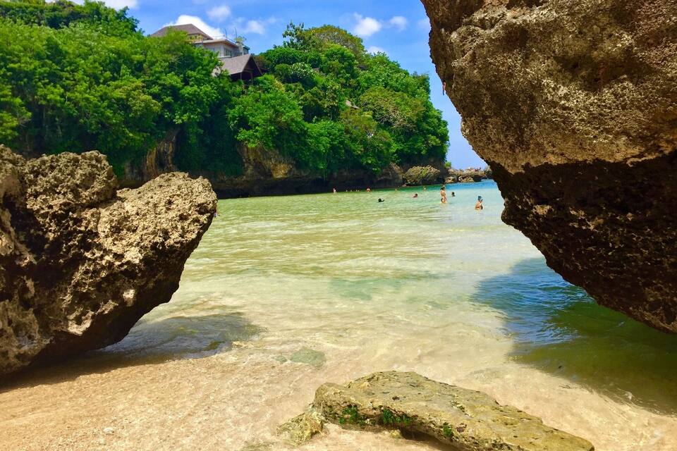 A beach with clear water, rocky formations, and lush greenery.
