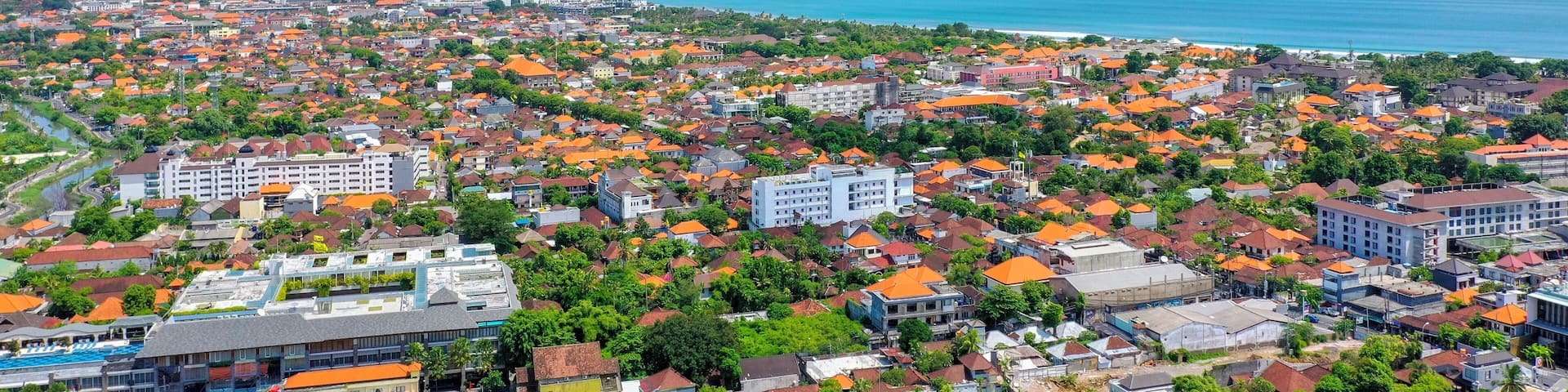 A coastal cityscape with orange-roofed buildings, a beach, and a clear blue sky.