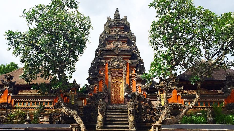 A traditional Balinese temple with ornate architecture, a central golden door, and a staircase leading up to it.