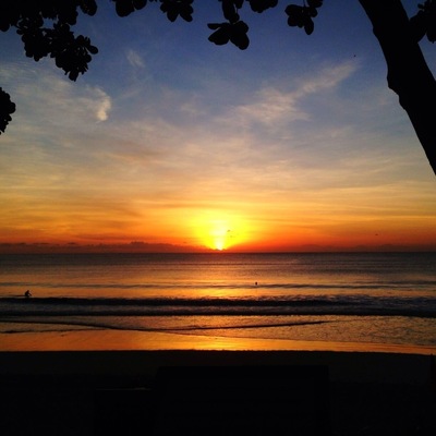 Un coucher de soleil sur l’océan, avec la silhouette d’une personne sur la plage.