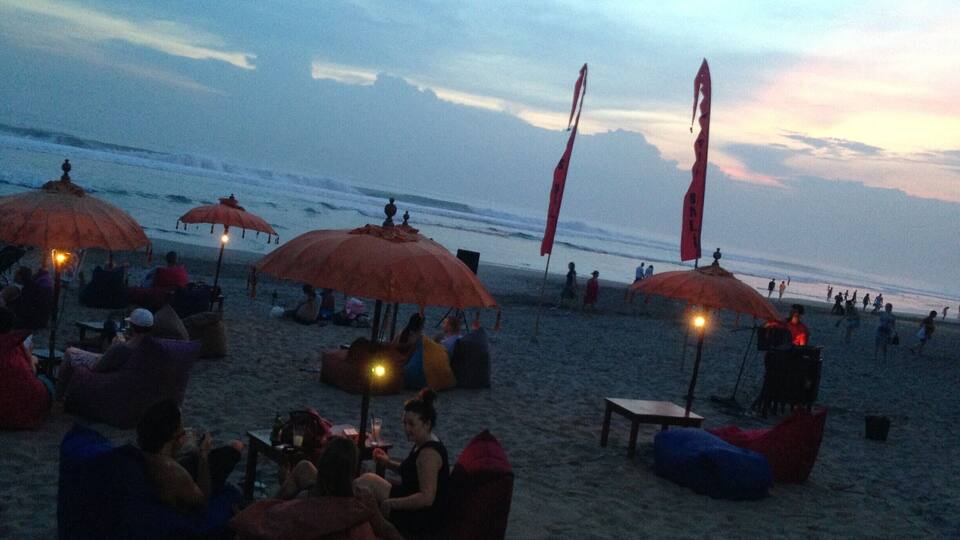 A beach with people sitting under umbrellas, some with tables and chairs.