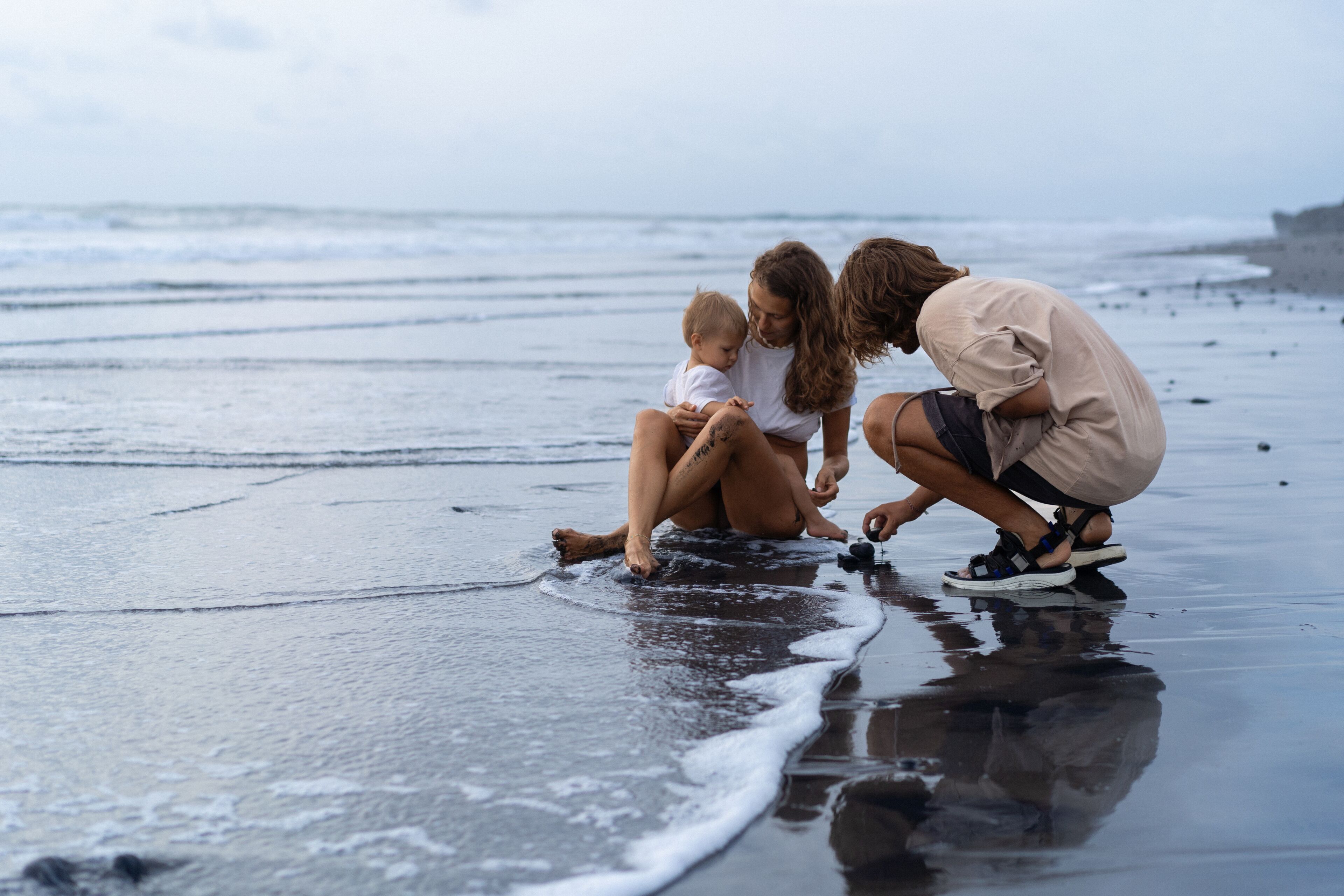 Uma família numa praia com ondas e uma costa rochosa.