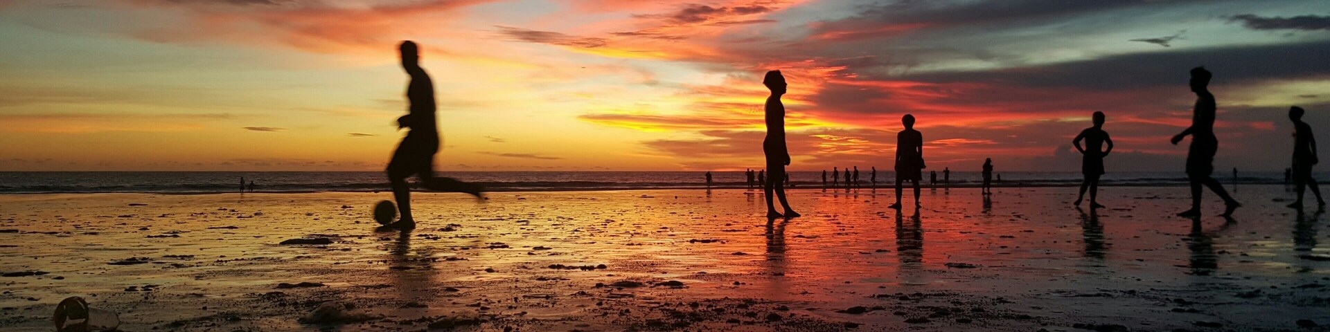 A beach at sunset with people playing soccer.