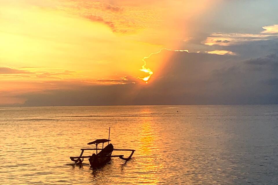 A sunset over a calm sea with a small boat in the foreground.