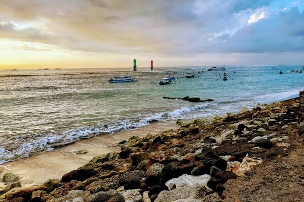 A rocky shoreline with boats in the water and a lighthouse in the distance.
