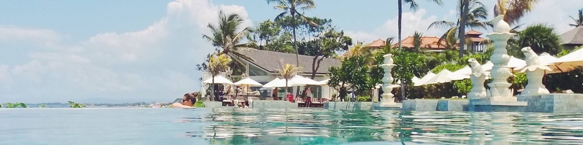 A clear blue pool with palm trees and a resort in the background.