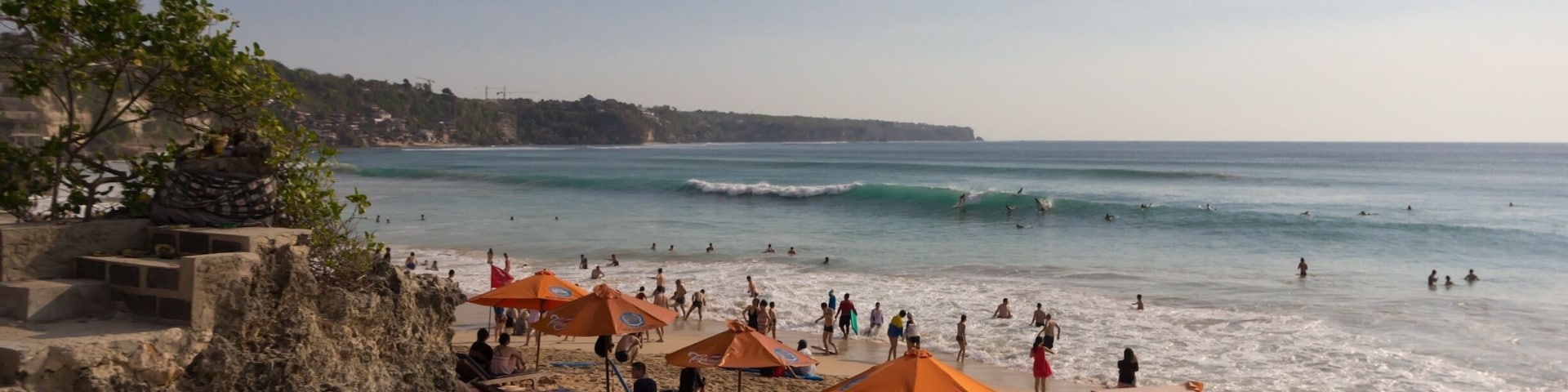 A beach with orange umbrellas, people swimming, and waves.