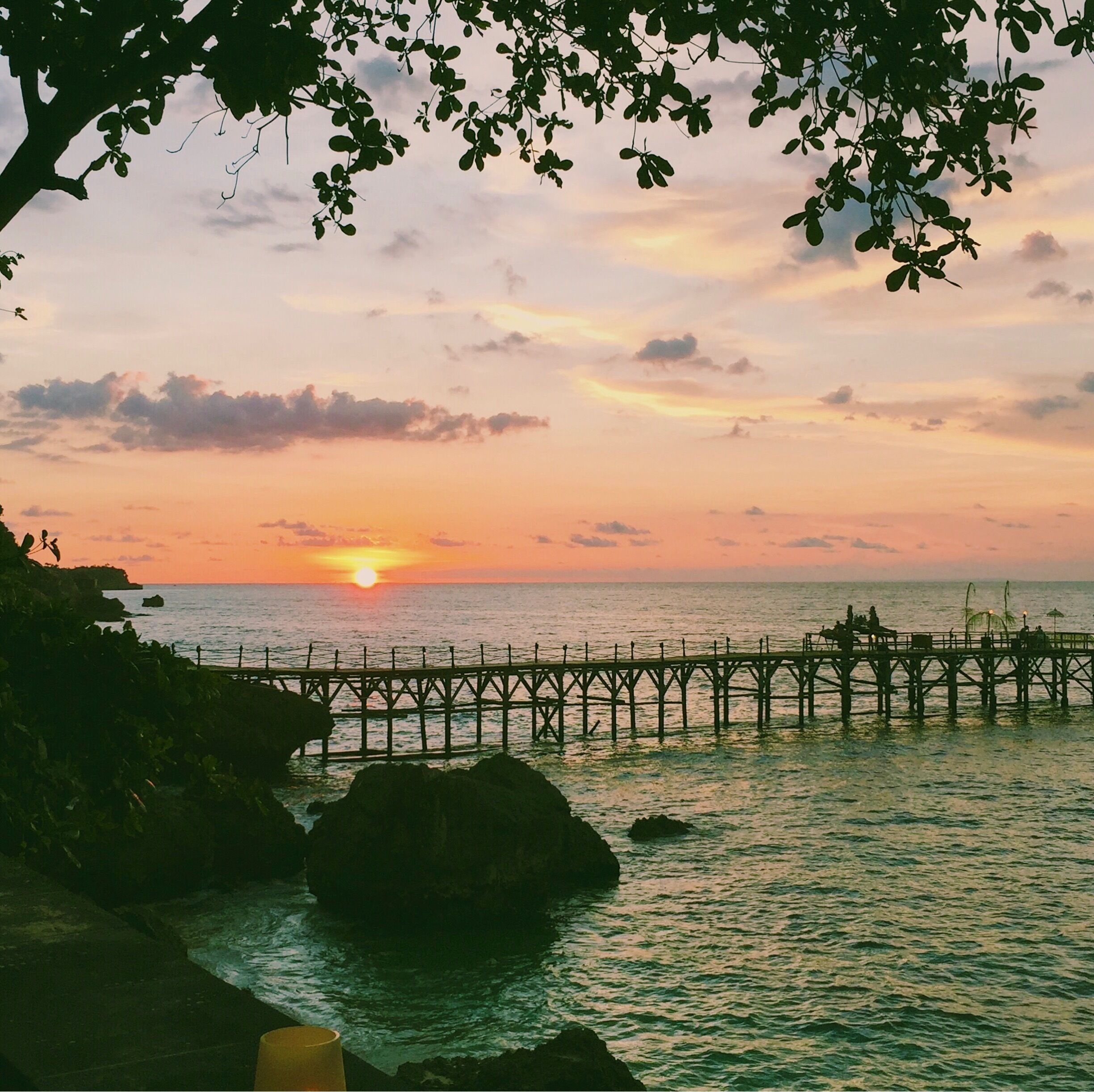 A sunset over the ocean with a pier extending into the water.