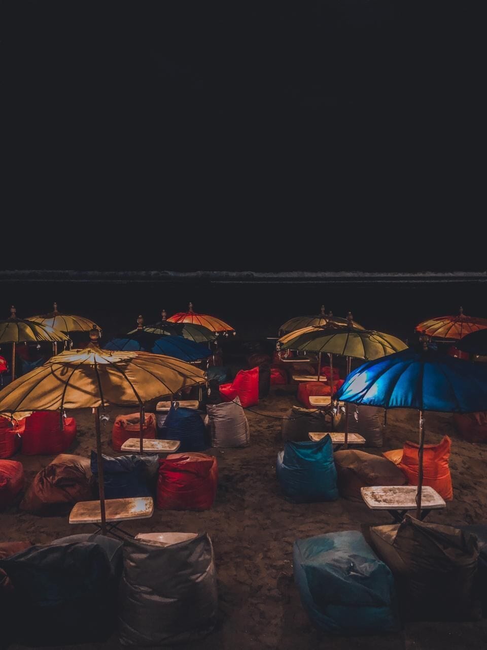 Ein Strand bei Nacht mit bunten Sonnenschirmen und Sitzsäcken.