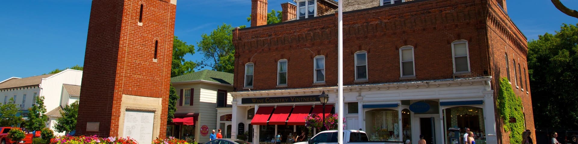 A historic town square with a clock tower, a flagpole, and a vintage storefront.