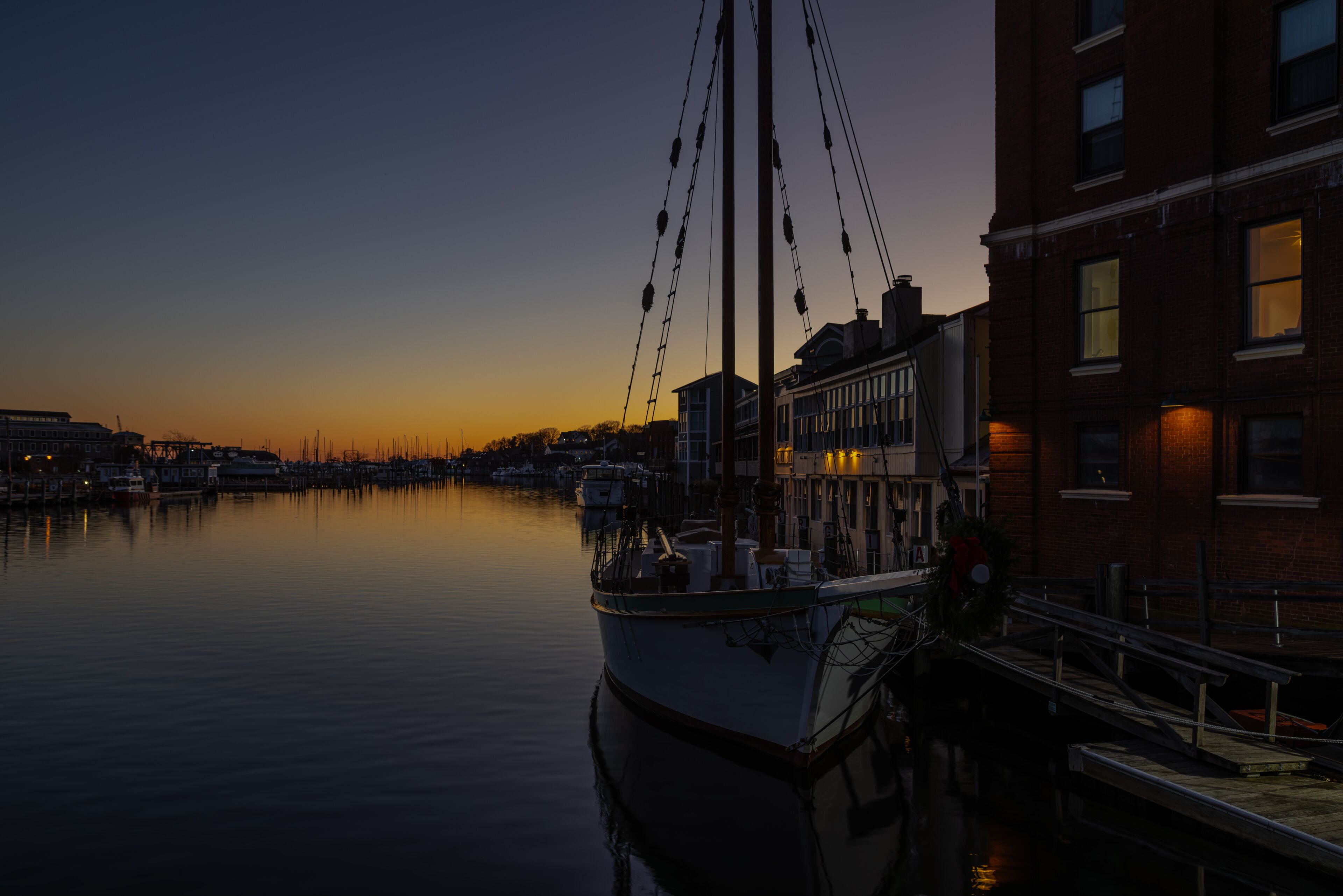 A calm harbor at dusk with a boat docked on the left and buildings along the right.