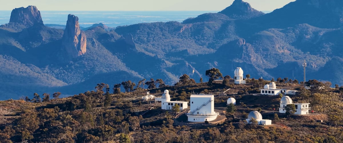 A mountainous landscape with several white observatory domes and a clear view of the ocean.