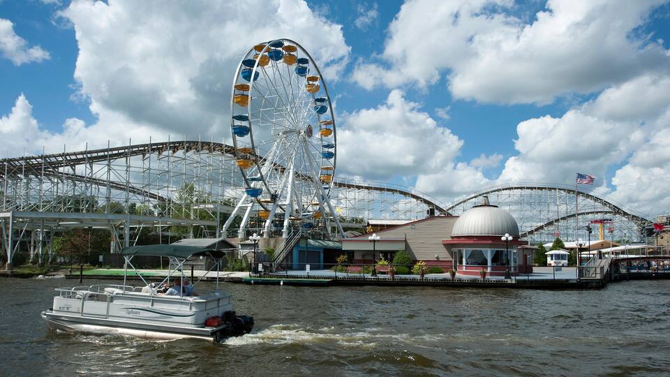 A Ferris wheel, a roller coaster, and a boat on a body of water.