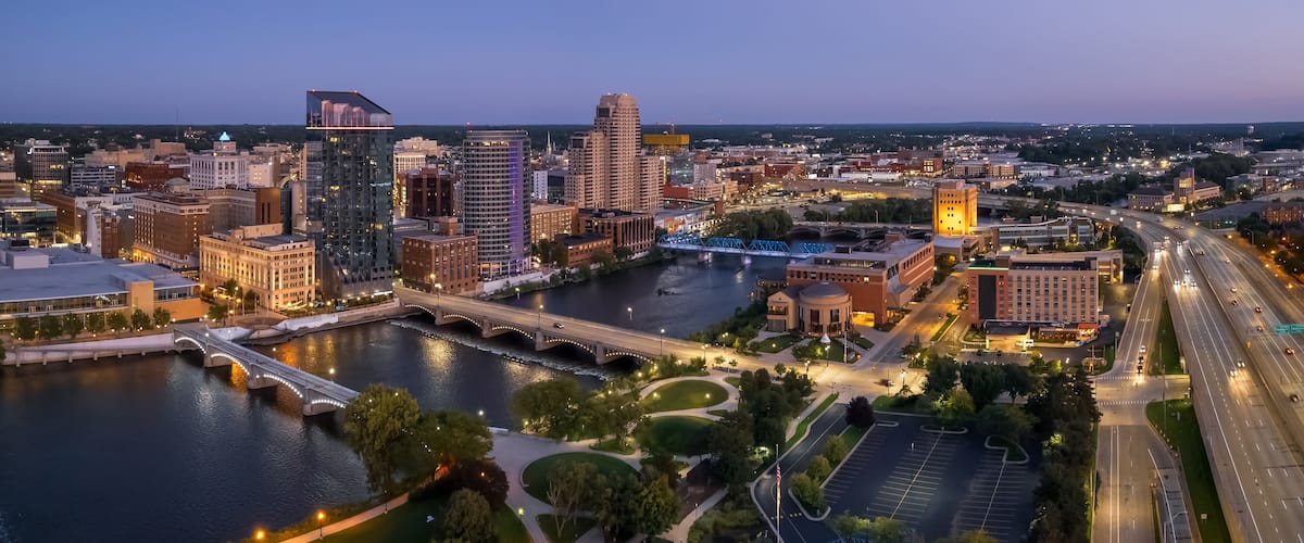 A cityscape at dusk with a river, bridges, and illuminated buildings.