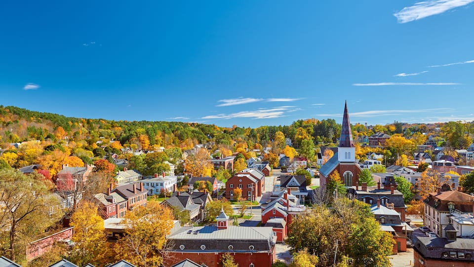 A town with autumn-colored trees, a prominent church steeple, and a mix of residential and commercial buildings.