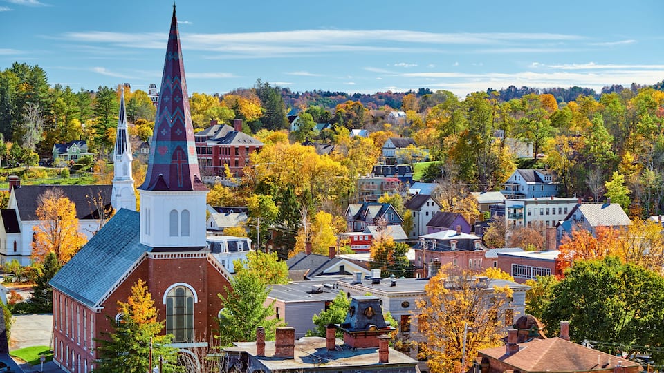 A town with a prominent church steeple, autumn-colored trees, and a mix of residential and commercial buildings.