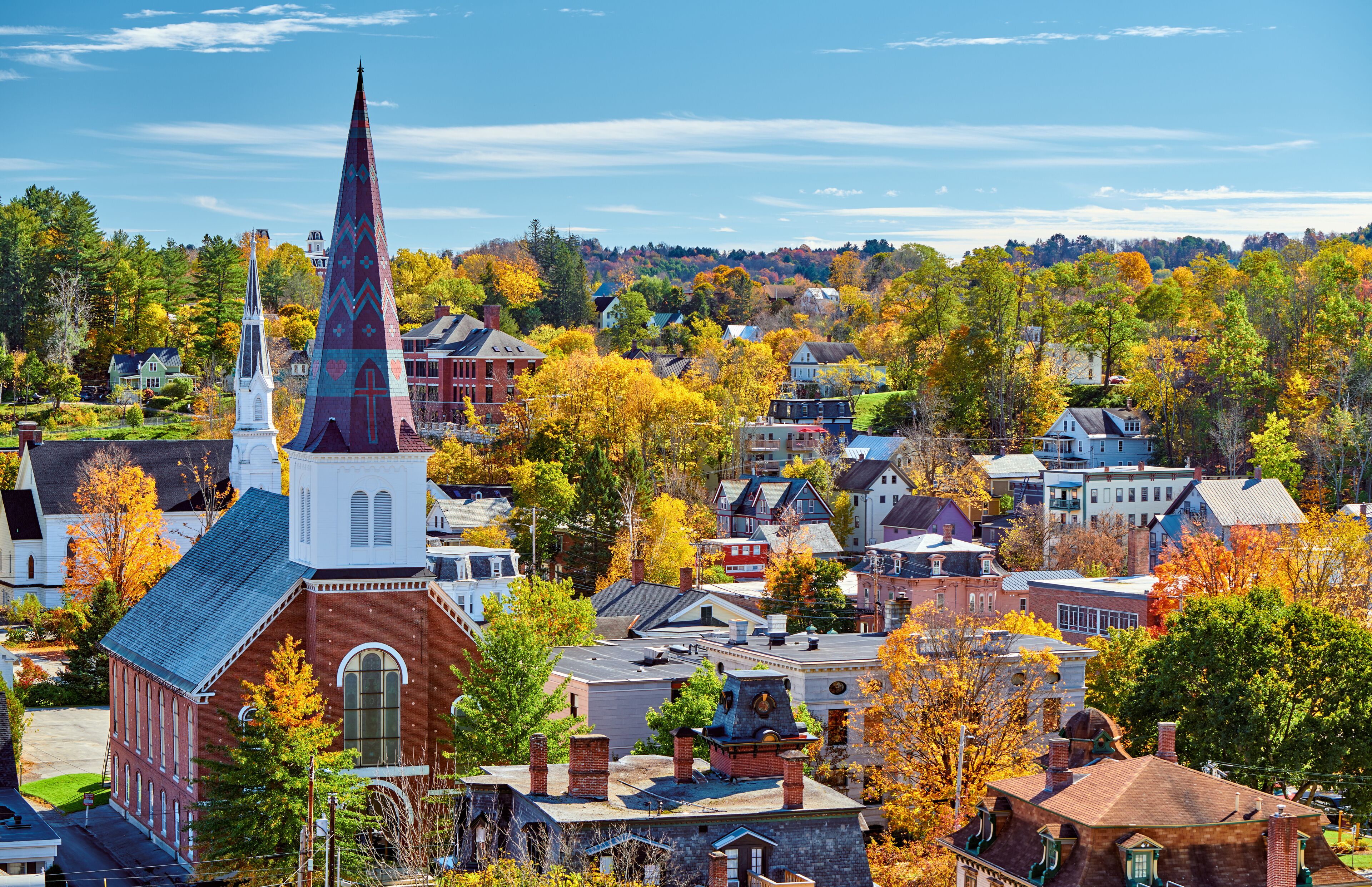 A town with a prominent church steeple, autumn-colored trees, and a mix of residential and commercial buildings.