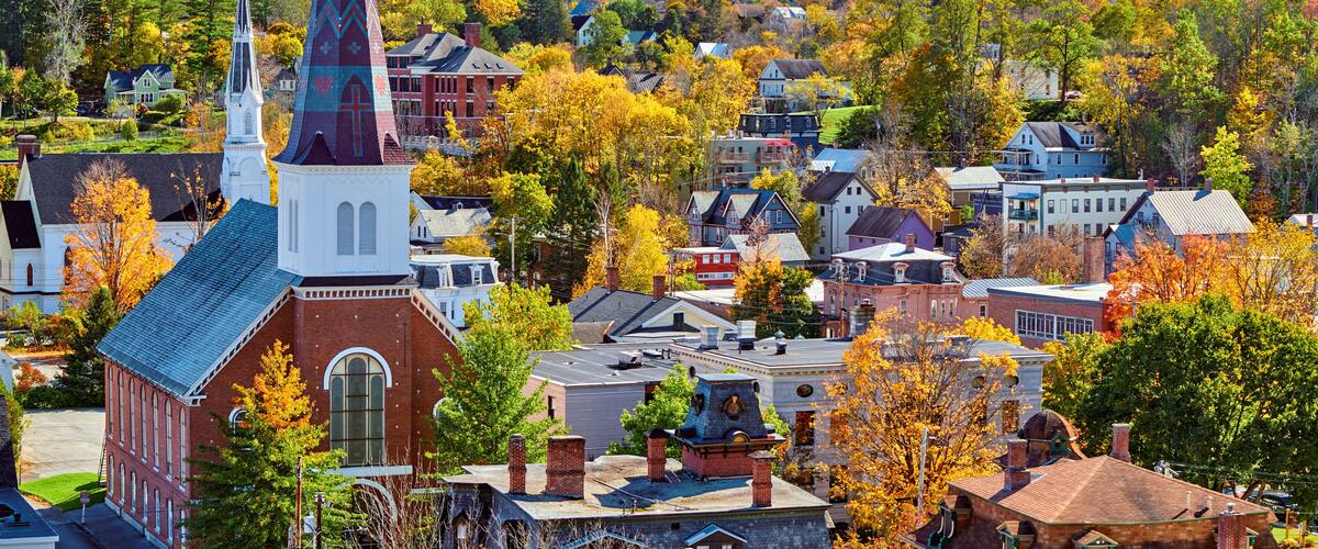 A town with a prominent church steeple, autumn-colored trees, and a mix of residential and commercial buildings.