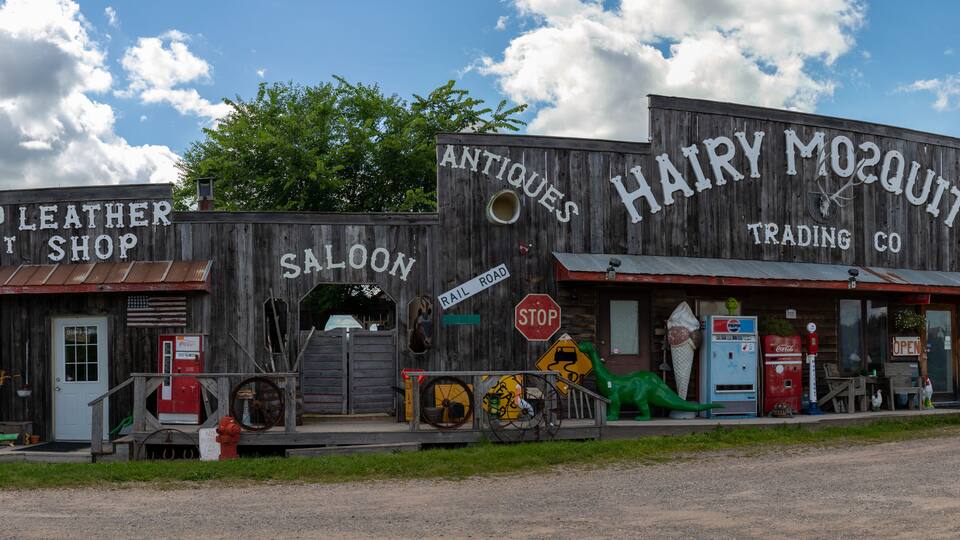 A rustic building with signs for 'Old Leather West Shop' and 'Hairy Moquott Trading Co.'