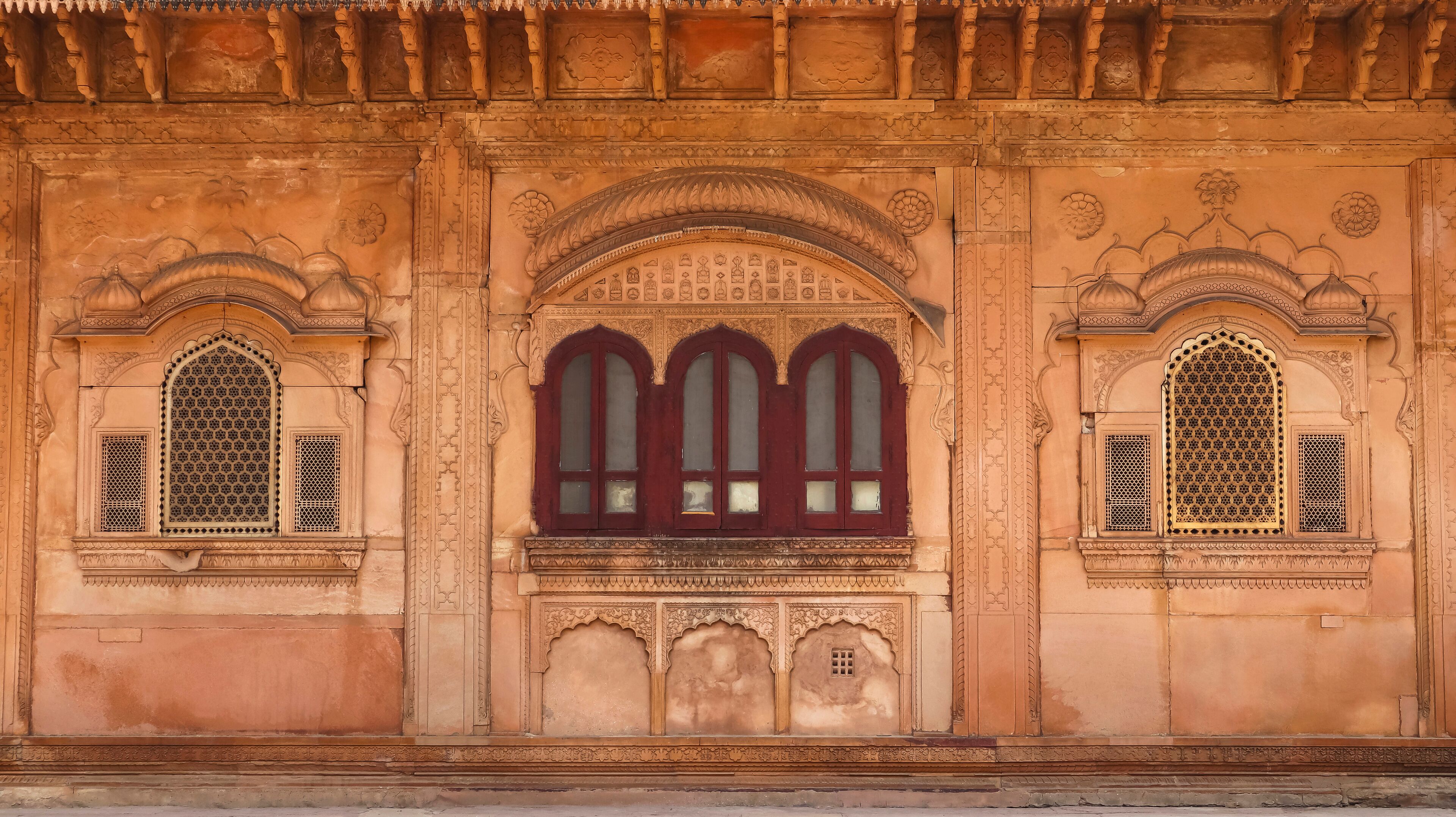 A building with intricate carvings and three arched windows with red frames.