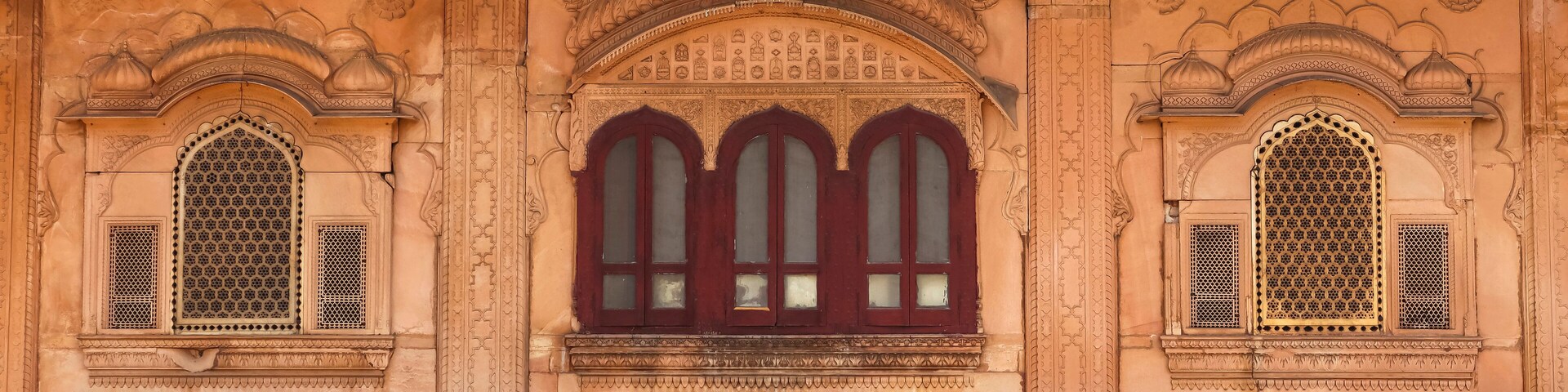 A building with intricate carvings and three arched windows with red frames.