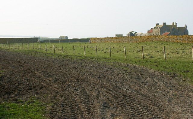 A plowed field, a fence, and a building in the background.